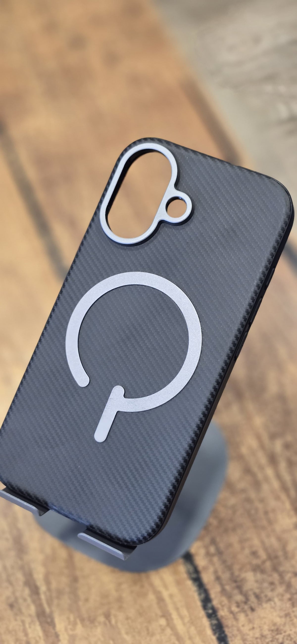 iPhone 16 black carbon-fibre style back case with magnetic ring on a stand